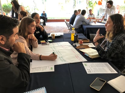 Group of people sat around a table in conversation. Note taking in progress. 
