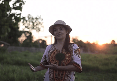 Women speaking to the camera. Fields in the background and the sun setting. 
