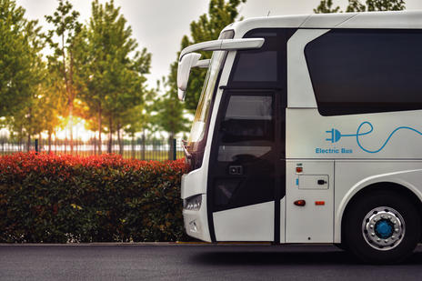 Side view of a coach on the road. Foliage and trees in the background with the sun setting.