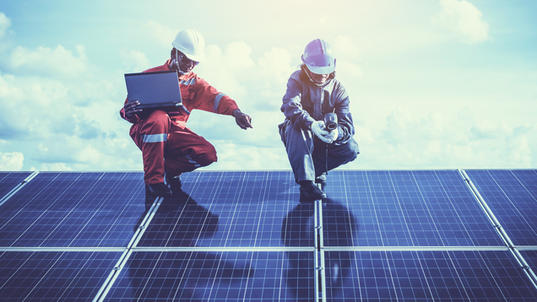 Two workers with hard hats crouching on solar panels