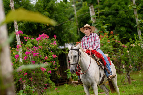 Photo of a young Peruvian farmer riding a horse. Trees and shrubs in the backdrop