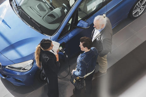 Aerial shot of three people in a car showroom standing next to a blue car